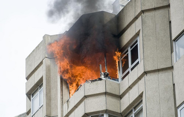 Grandes llamas saliendo del último piso del edificio, con una gran humareda negra.