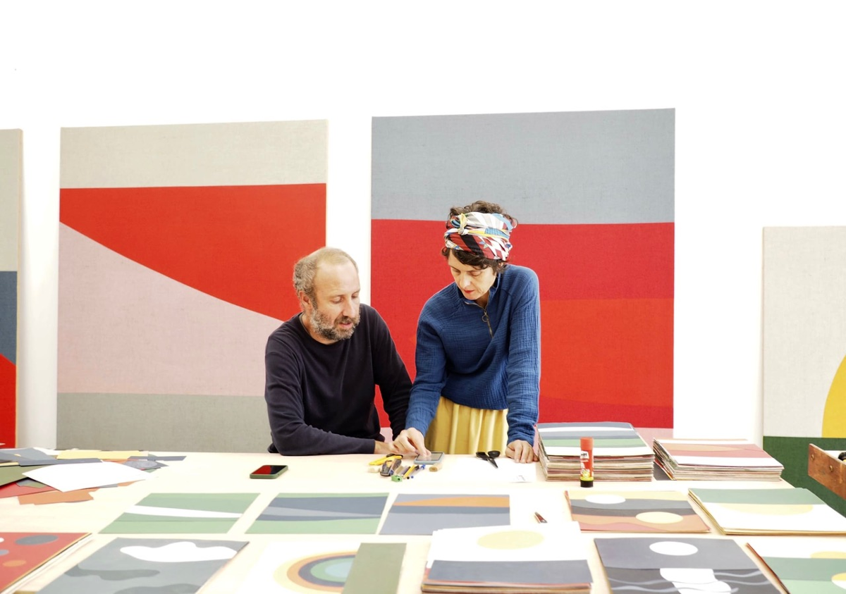 Ana Ausín y Antonio Ballester hablando delante de varios cuadros apoyados en una mesa