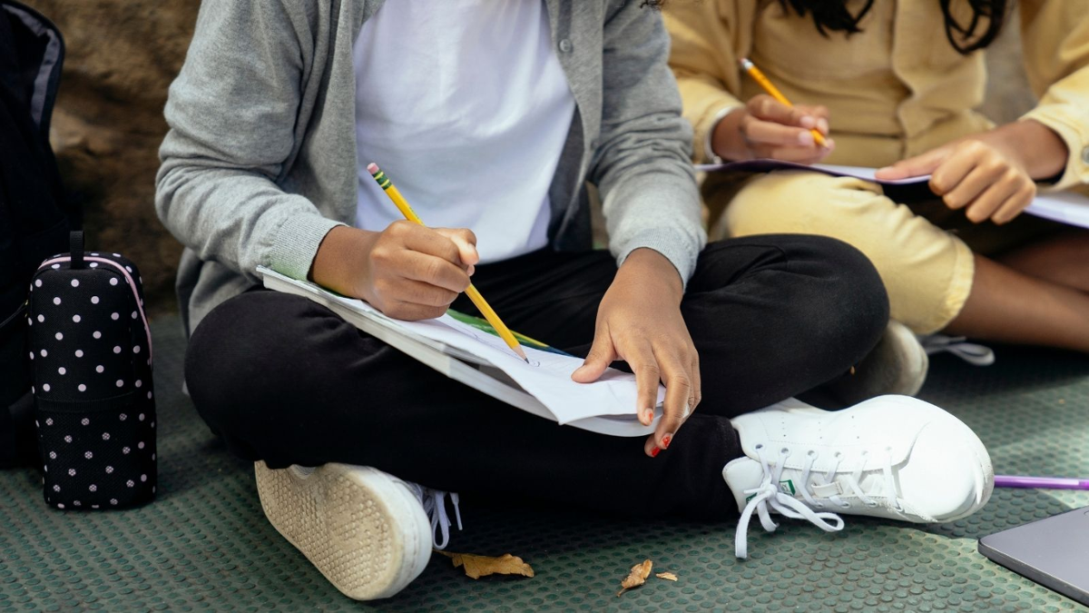 Nenos sentados no chan debuxando nun caderno