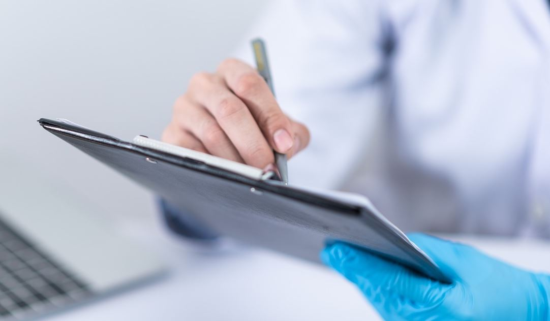 Persoa con bata e luvas desechables enchendo un docuemento.