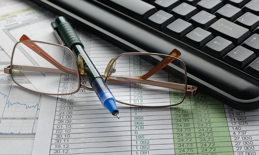 Documentos con datos e gráficos, lentes, bolígrafo e computador.