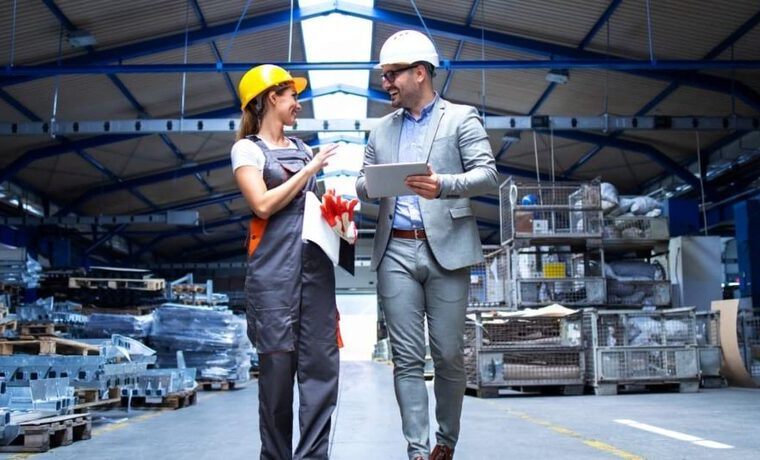 Dúas persoas, un inspector e unha traballadora dentro dunha nave industrial falando