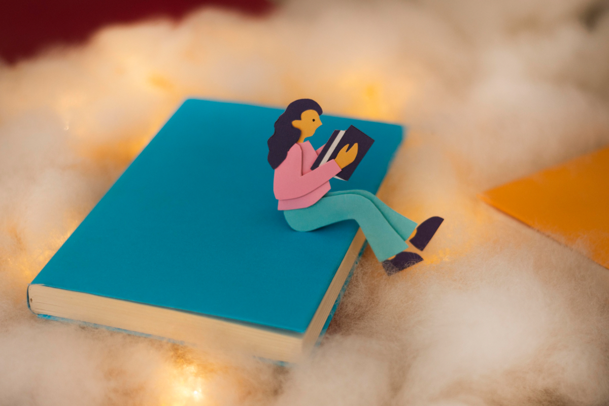 Ilustración de persona leyendo sentada  sobre un libro 