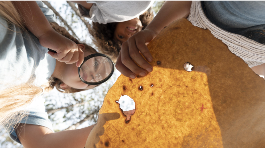 Fotografía de unos niños mirando un mapa con una lupa.