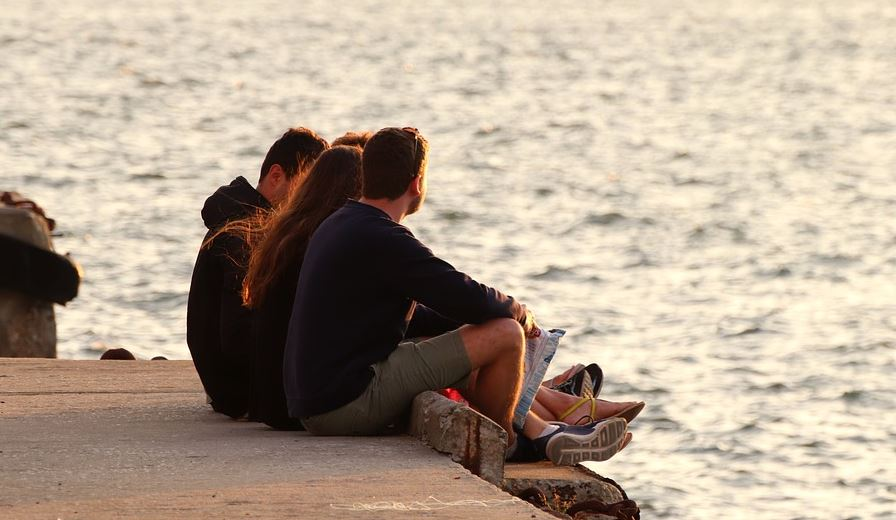 Xente nova sentada xunto ao mar. 