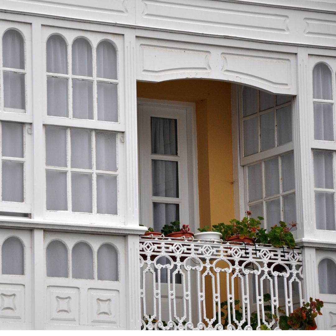 Fotografía dunha casa cunha galería e un pequeno balcón con flores.