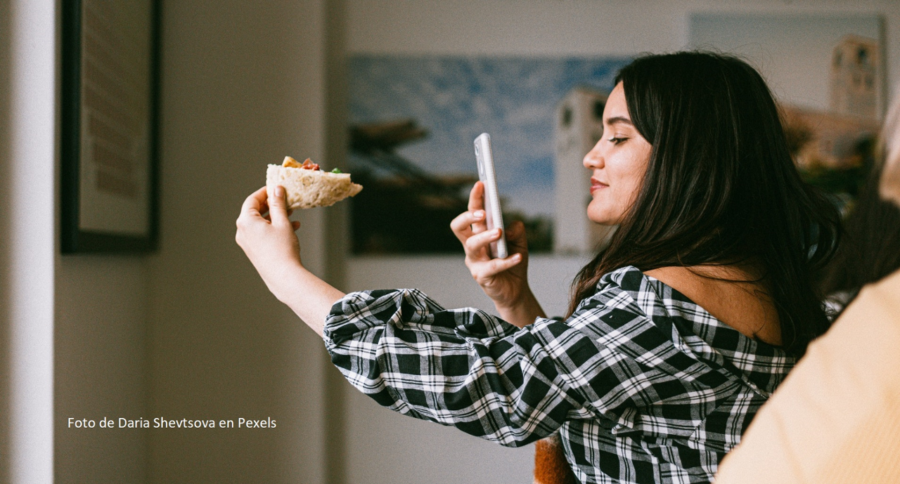 Una mujer fotografiando un bocadillo con el móvil en el interior de una casa