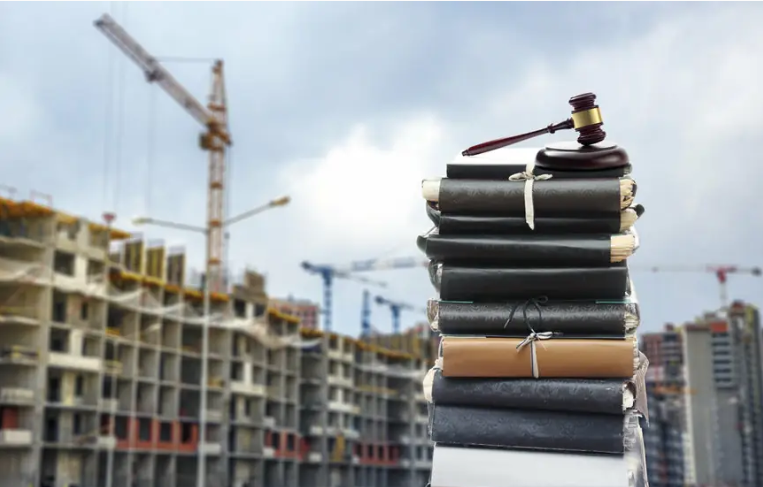 Edificio en construción e uns libros e un martelo de xuez diante.