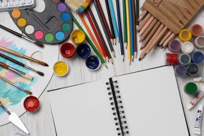 Una libreta abierta rodeada de varios utensilios de dibujo y pintura